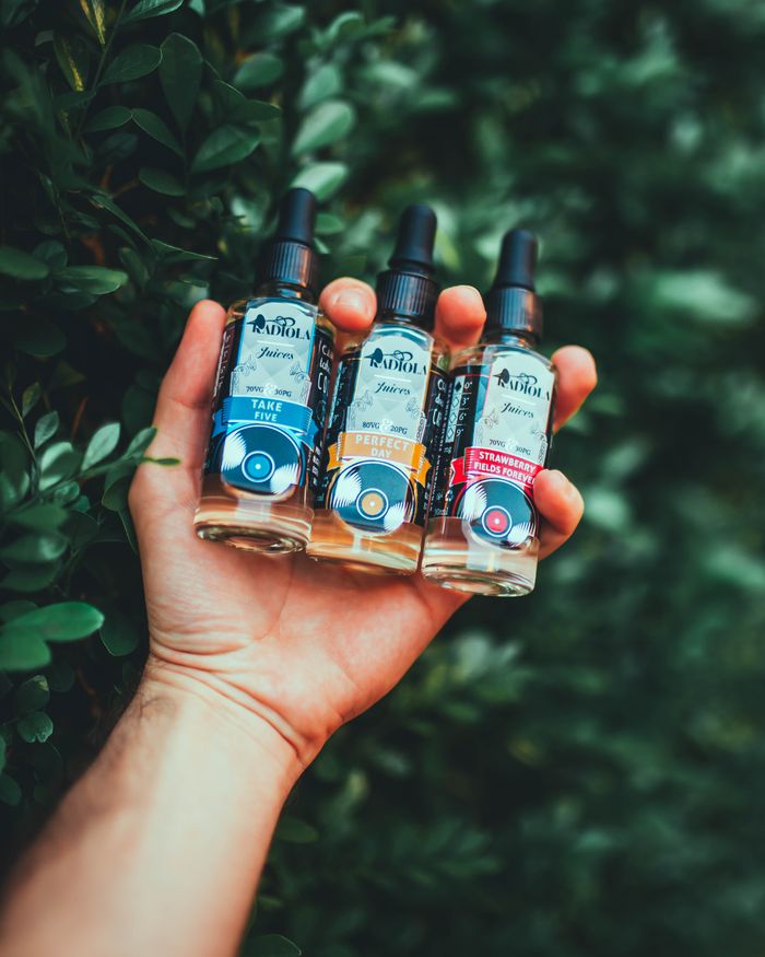 Services A close-up of a hand holding three Radiola vape juice bottles against a leafy background.
