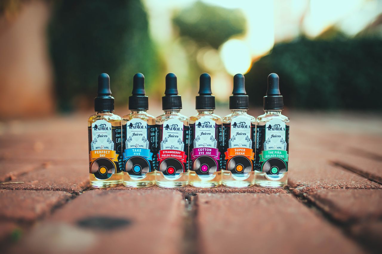 Services Vibrant vape juice bottles arranged on a brick pathway outdoors in a row.