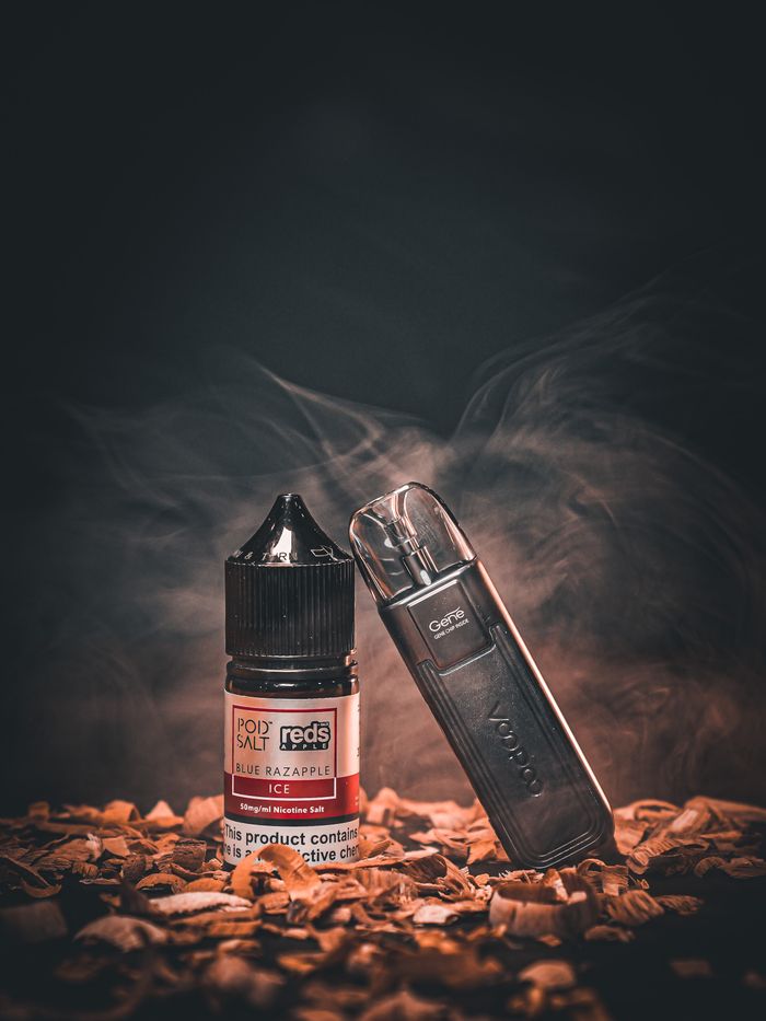 Services A vape pen and e-liquid bottle placed on carved wood amidst swirling smoke.